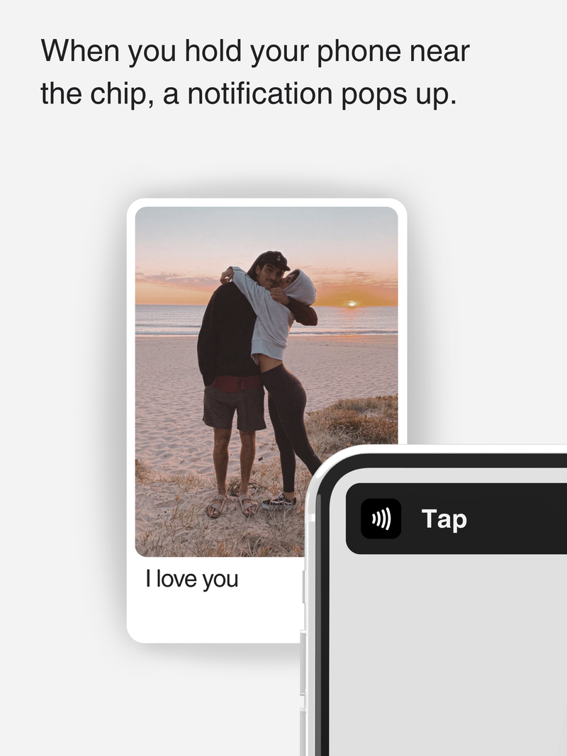 When you hold your phone near the chip, a notification pops up. Personalized NFC card featuring a couple hugging at sunset with “I love you” text and a phone tap notification.